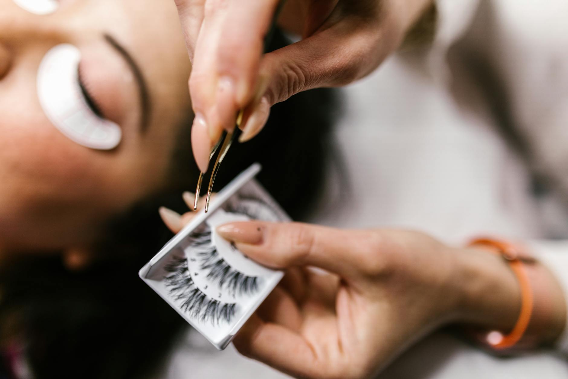 close up shot of a person holding a tweezer and false eyelashes